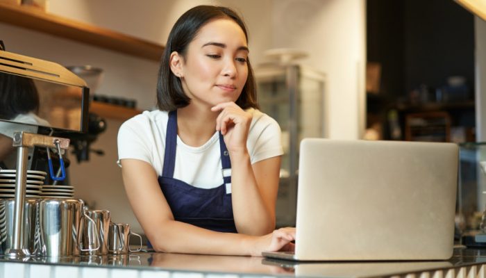 retrato-de-uma-sorridente-barista-coreana-em-uma-cafeteria-parada-no-balcao-com-um-laptop-sorrindo-e.jpeg
