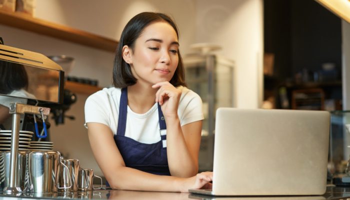 retrato-de-uma-sorridente-barista-coreana-em-uma-cafeteria-parada-no-balcao-com-um-laptop-sorrindo-e.jpeg