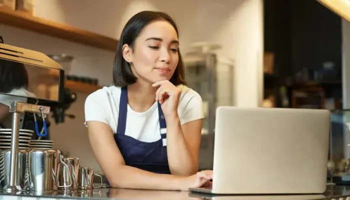 retrato-de-uma-sorridente-barista-coreana-em-uma-cafeteria-parada-no-balcao-com-um-laptop-sorrindo-e.webp